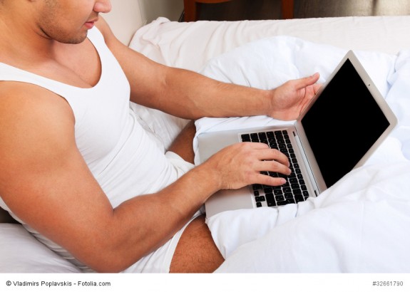 Mann mit Laptop im Schlafzimmer